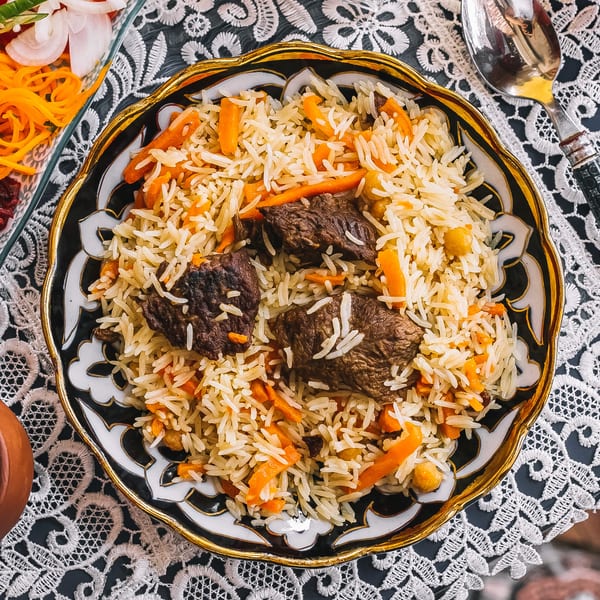 A close-up of a colorful rice pilaf dish with meat, carrots, and chickpeas in a decorative bowl.