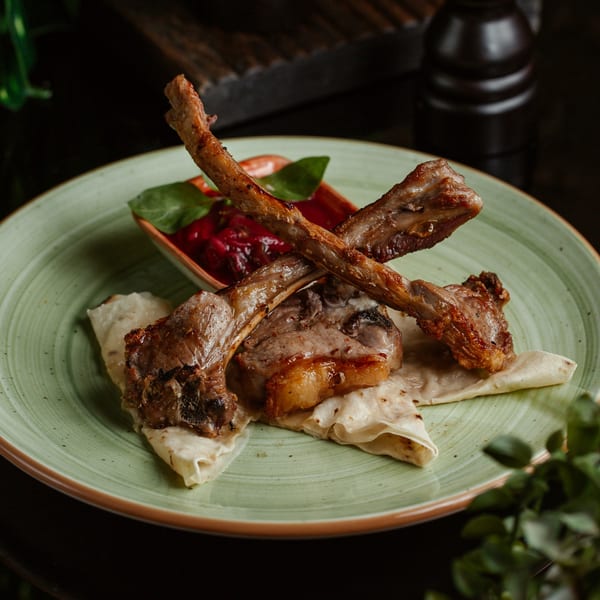 Grilled lamb chops with a side of red sauce and flatbread on a light green plate.