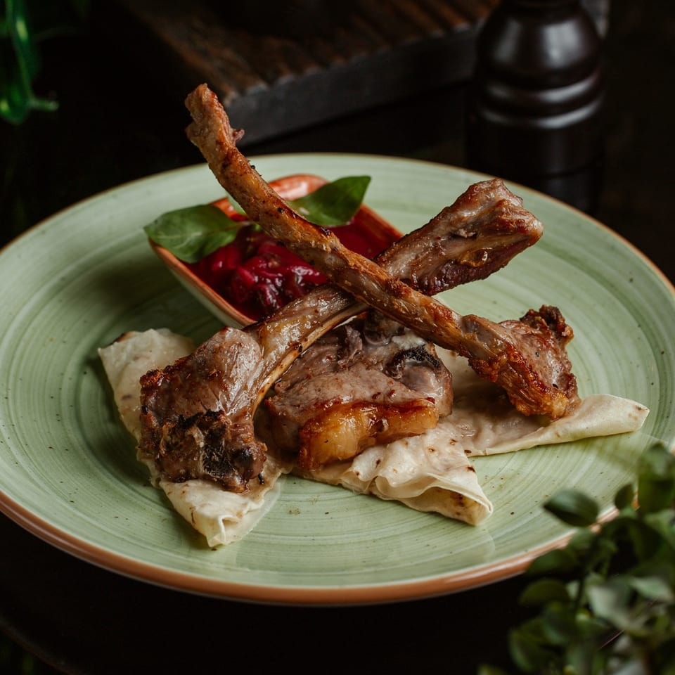 Grilled lamb chops with a side of red sauce and flatbread on a light green plate.