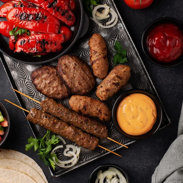 Grilled halal kabobs, patties, and sausages with roasted red peppers, onions, and sauces on a platter.
