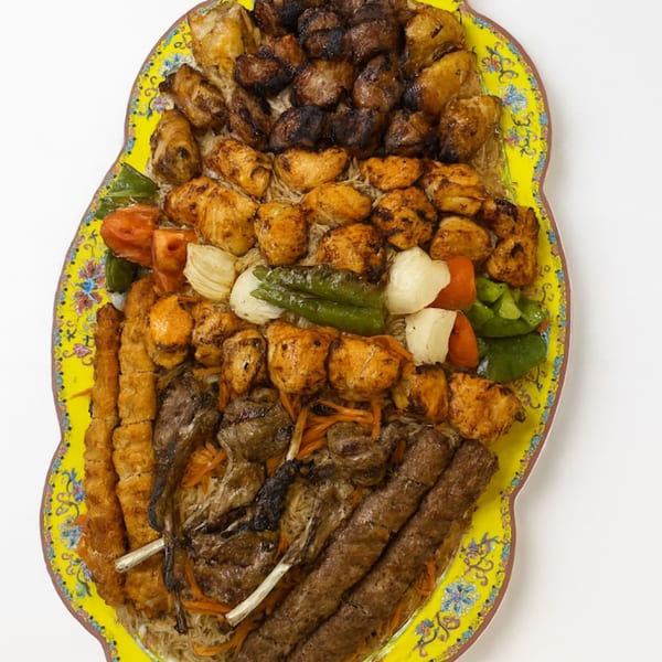 A large platter of grilled halal meats, including chicken, lamb, and beef kabobs, with vegetables and rice.